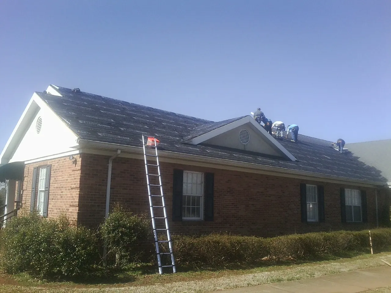 Crew tearing shingles off a brick ranch roof with a ladder set — Metal Roof Repair work by our crew in Royal City