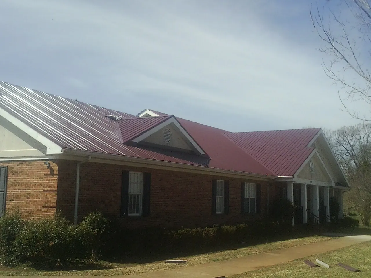 Red metal roof with gabled entries on a long brick building, from a Hail Damage Roof Repair job in Royal City