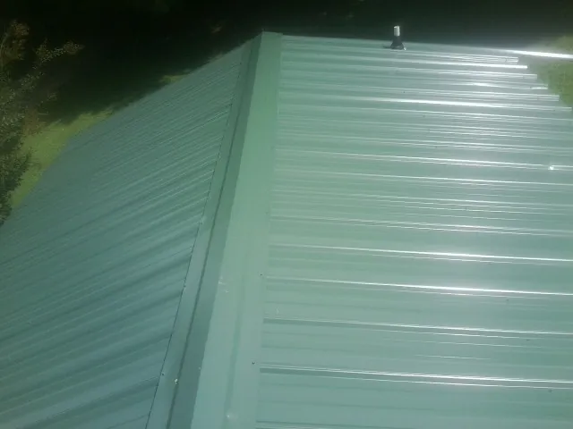 New green metal panels meeting at the ridge of a roof — Flat Roof Repair work by our crew in Royal City