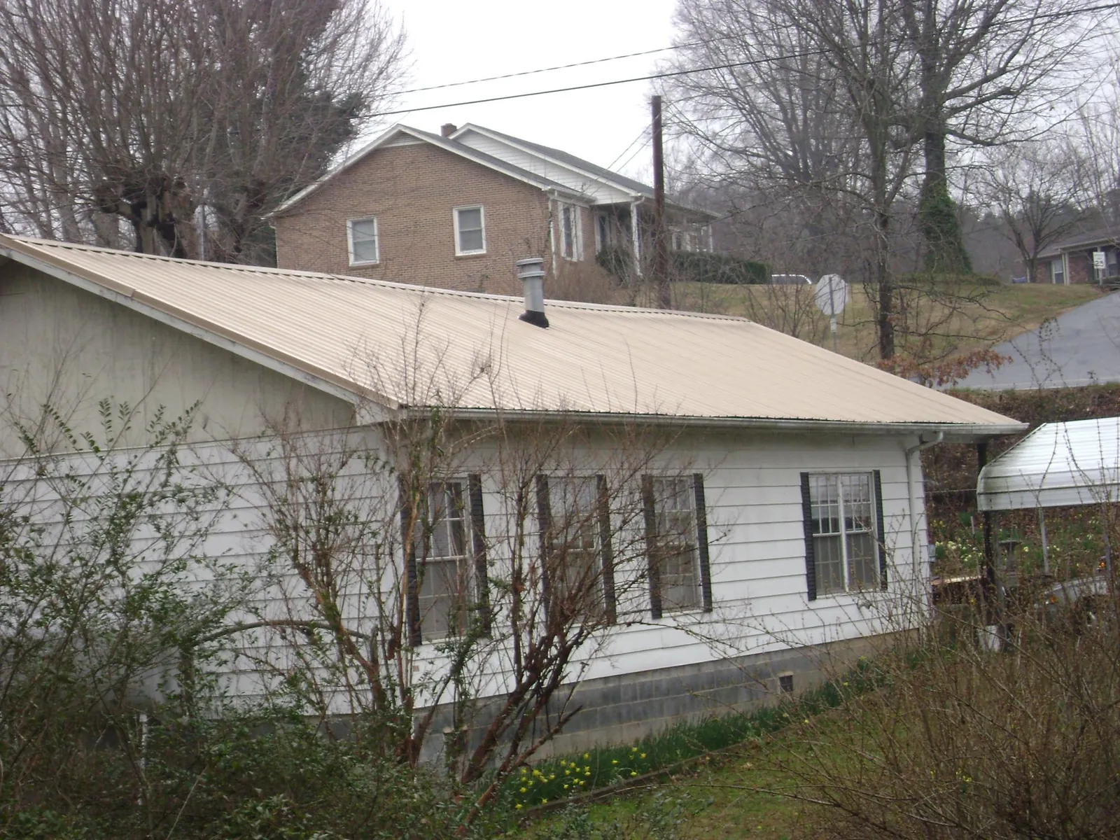 Tan metal roof on a white sided house set into a hillside — Commercial Roofing by Roofing Brothers in Royal City